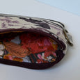 A close-up of a zippered pouch with a cream-colored exterior featuring a purple and black floral pattern, and a vibrant red, orange, and brown floral lining. The pouch is shown open on a clean white surface.